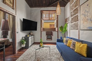Un salon confortable avec un canapé bleu, un téléviseur à écran plat, une table basse et un escalier menant à un niveau supérieur.