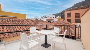 Une terrasse sur le toit, avec une table et des chaises blanches, entourée d’immeubles aux toits de tuiles.