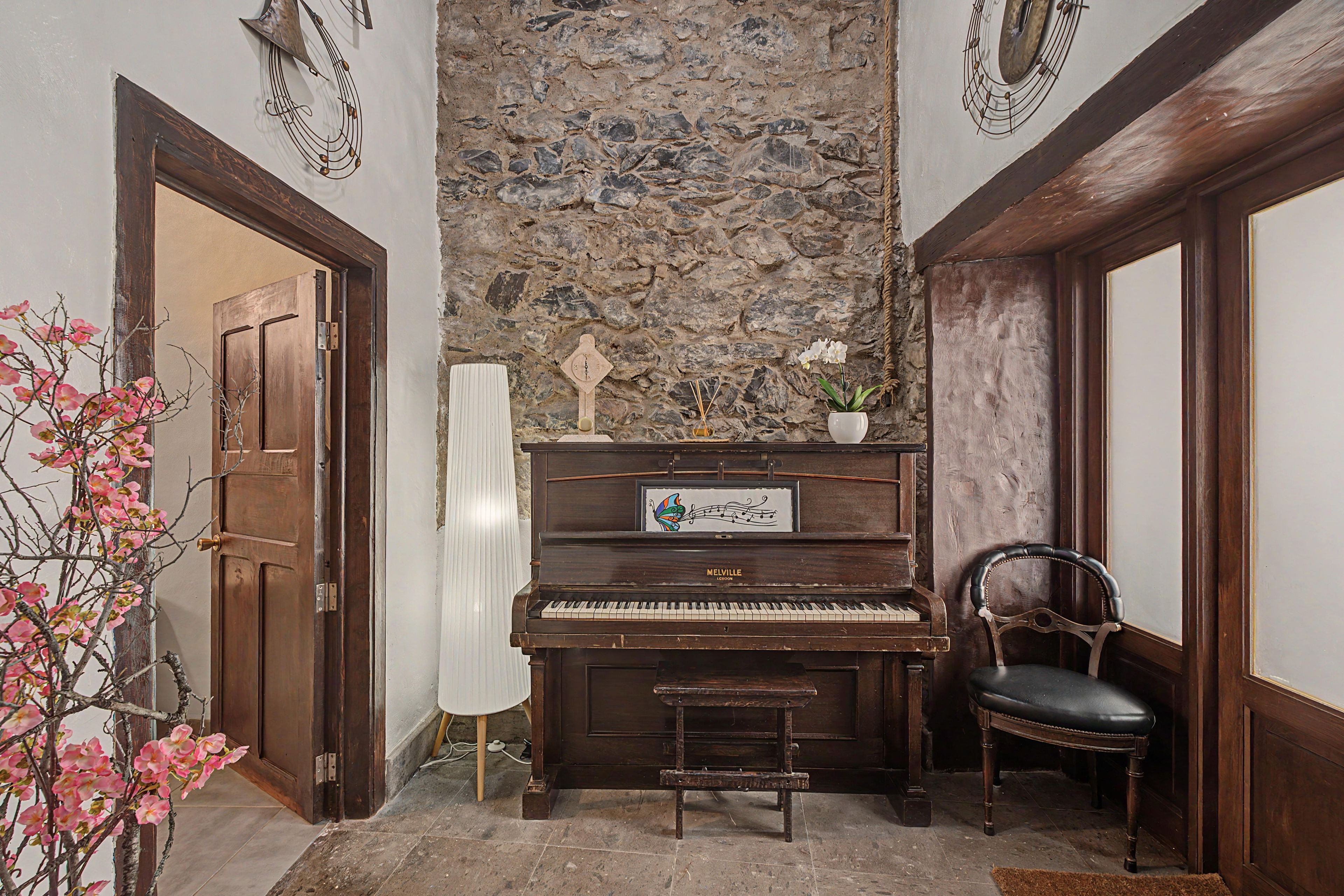 Een kamer met een piano, een stoel, een wandklok en decoratieve wandpanelen.