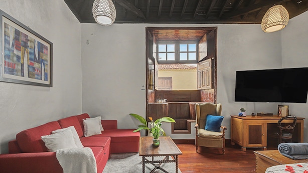 Una sala de estar con un sofá rojo, una mesa de centro, un televisor y un mueble de madera.