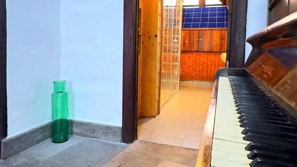 Un piano en una habitación con suelo de baldosas y un vano que conduce a otra habitación con pared de azulejos azules y un armario de madera.