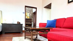 Una sala de estar con un sofá rojo, una mesa de centro de madera, un tapete blanco, un mueble de madera oscura y una chimenea de piedra.