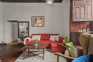 Un salon avec un canapé rouge, une table basse, un miroir et un tableau accroché au mur.