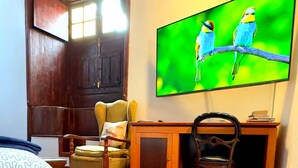 Una habitación con escritorio de madera, una silla, una cama con ropa de cama estampada y un televisor mostrando aves.