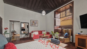 Una habitación amplia con una cama grande, un sofá rojo, una silla de madera y una mesa de comedor.