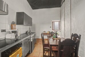 Una cocina con estufa, lavamanos y una mesa de comedor con sillas.