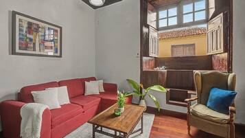 Una sala de estar con un sofá rojo, una mesa de centro de madera y un sillón de mimbre.