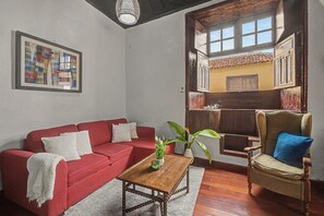 Una sala de estar con un sofá rojo, una mesa de centro de madera y un sillón de mimbre.