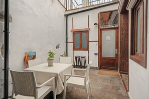 Un pequeño patio al aire libre con una mesa, sillas, una planta en maceta y una puerta de madera.