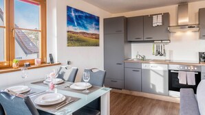 Una cocina moderna con armarios grises, horno empotrado y comedor con mesa lista para dos.