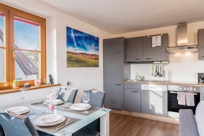 Une cuisine moderne avec des meubles gris, un four encastré et un coin repas avec une table dressée pour deux personnes.