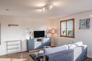 Un salon moderne avec un téléviseur à écran plat, un canapé gris, une petite table basse, un lampadaire et une fenêtre donnant sur un beau paysage.