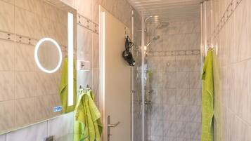 Une salle de bain moderne avec une douche à parois de verre, un miroir avec éclairage intégré et une serviette verte accrochée au mur.