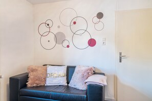 Une pièce avec un canapé en cuir noir, un mur orné de motifs circulaires abstraits et une porte.