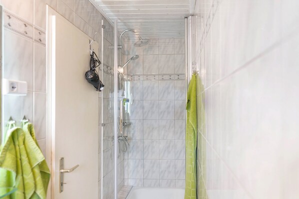 A shower with a glass door, a towel rack with a towel, and a green shower curtain.