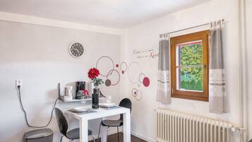 Un coin repas avec une table blanche, des chaises noires, une horloge, un radiateur et une fenêtre avec des rideaux.