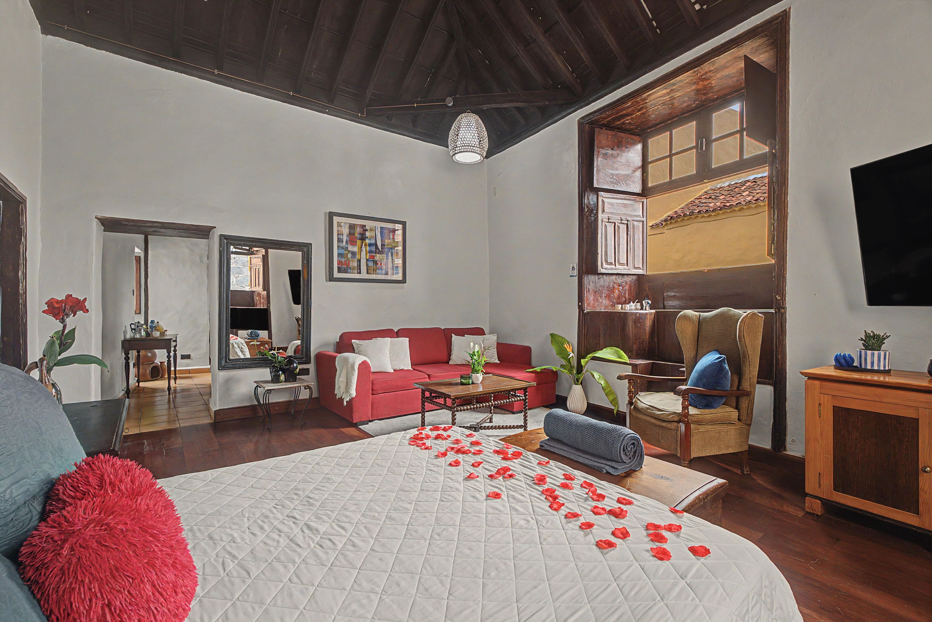A spacious room with a large bed, a red sofa, a wooden chair, and a dining table.
