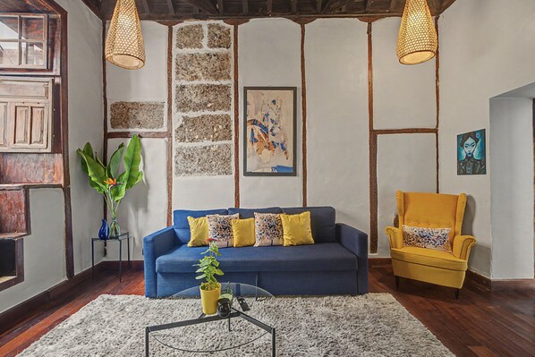 Une pièce avec un canapé bleu, un fauteuil jaune, une table basse et une grande plante.