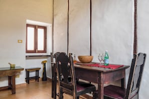 A dining area with a wooden table, chairs, a window, and a small table with a bowl and a bottle.