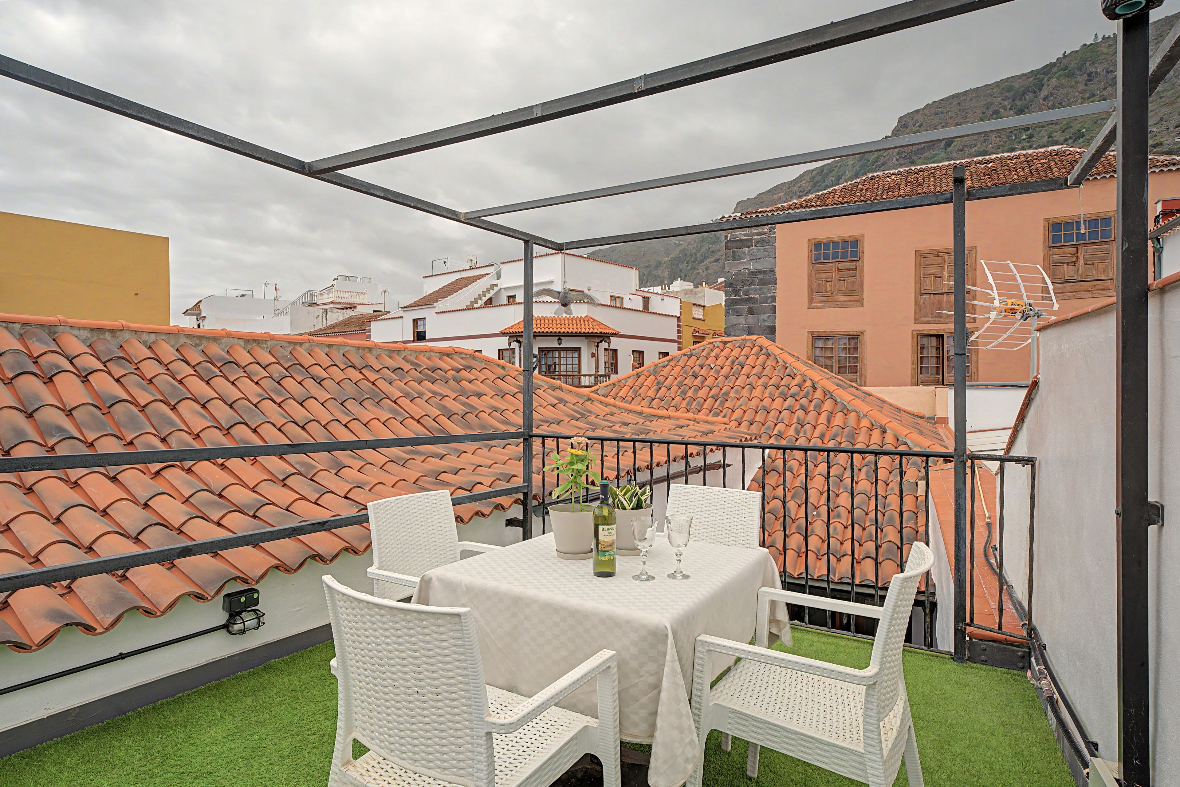An outdoor terrace with a table and chairs, surrounded by buildings with terracotta roofs.