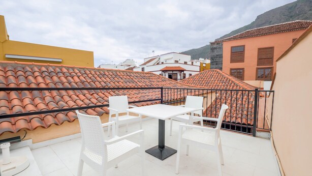 Um terraço no telhado com mesa e cadeiras brancas, cercado por edifícios com telhados de terracota.