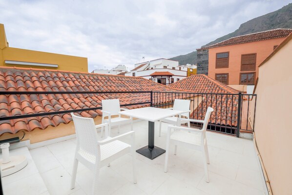 Eine Dachterrasse mit einem weißen Tisch und Stühlen, umgeben von Gebäuden mit Terrakotta-Dächern.