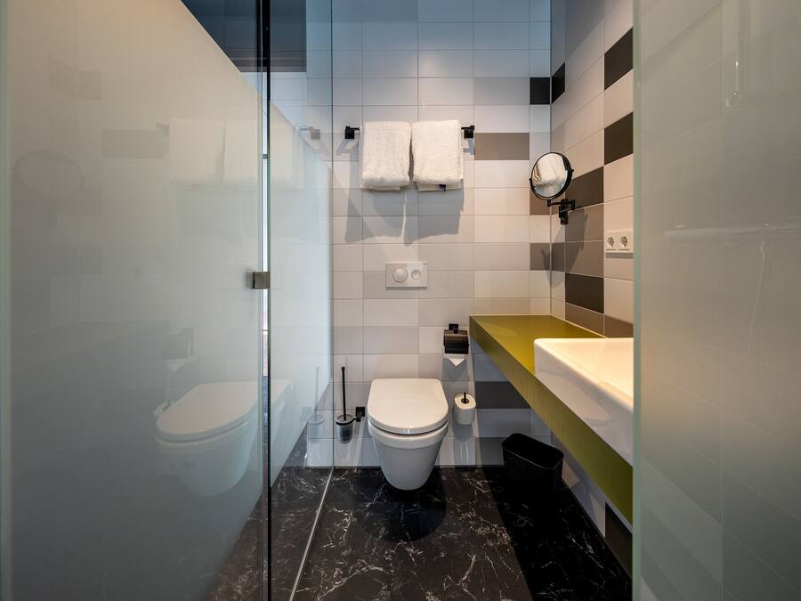 Ein modernes Badezimmer mit Duschkabine aus Glas, einer weißen Toilette, einem Marmorboden und einem gelben Waschtisch mit Spiegel.