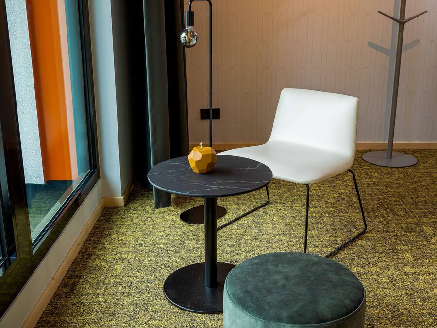Una habitación moderna con una mesa redonda, una silla blanca y un reposapiés verde.