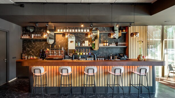 Een moderne bar met een marmeren aanrecht, barkrukken en diverse flessen en glazen.