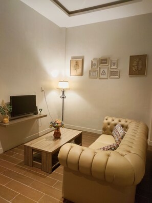 A living room with a television on a shelf, a lamp, a sofa, and a coffee table. - Green Forest Hotel (Tebing Tinggi)