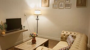A living room with a sofa, a coffee table, a TV on a stand, a floor lamp, and framed artwork on the wall. - Green Forest Hotel (Tebing Tinggi)