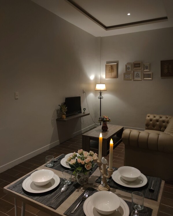 Ein Essbereich mit einem Tisch für vier Personen, einem Fernseher, einer Lampe und einer Couch.