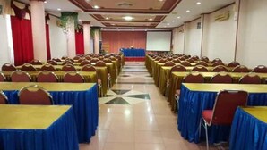 A conference room with rows of tables and chairs, a stage at the front, and a tiled floor. - Hotel Parewisata (Parepare)