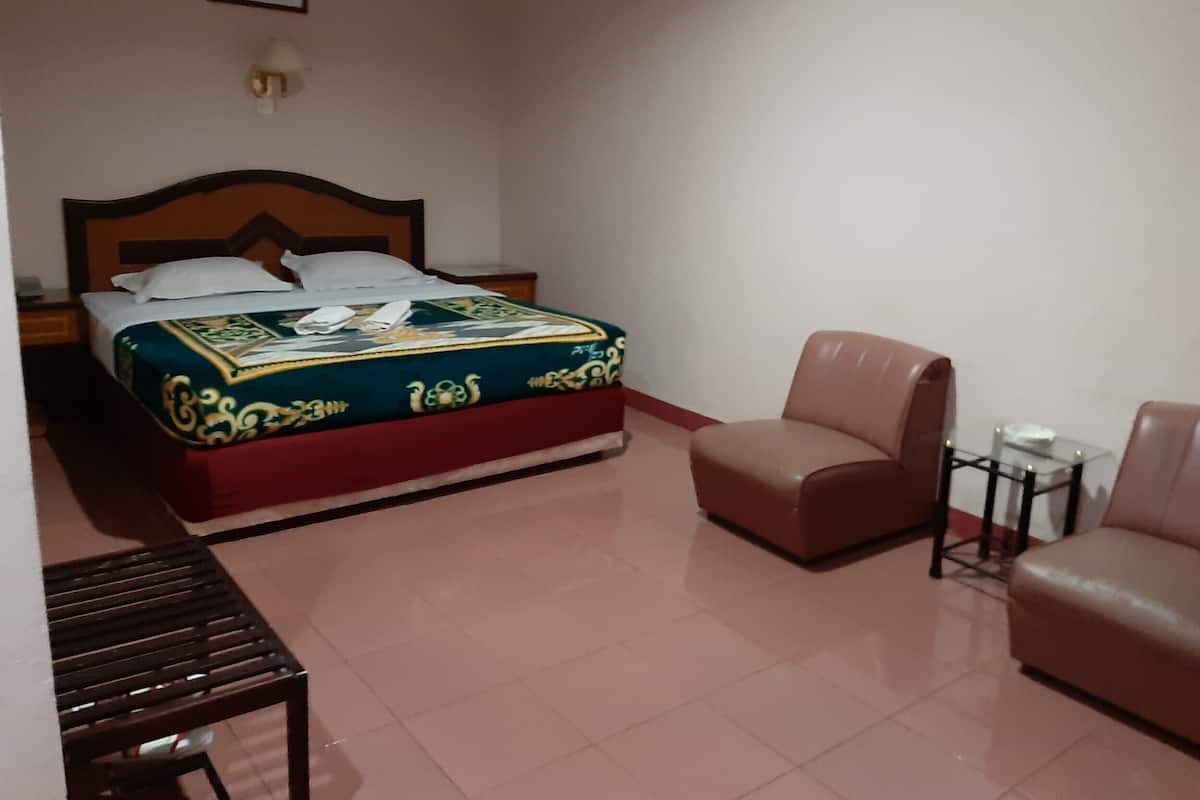 A bedroom with a bed, a chair, a small table, and a nightstand.