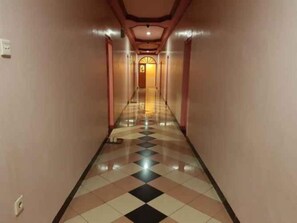 Pasillo de hotel con piso de diseño a cuadros, una fuente de luz central y una puerta al final.