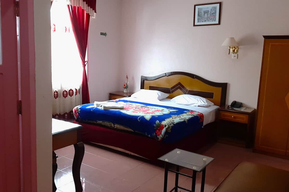 A bedroom with a bed, a bedside table, a nightstand, a lamp, and a door.