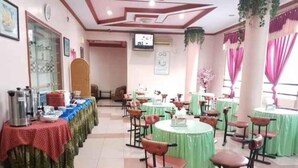 A dining area with round tables and chairs, a buffet setup on the left, and a television mounted on the wall. - Hotel Parewisata (Parepare)