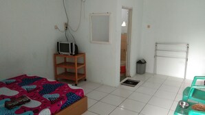 A room with a bed, a TV on a wooden stand, a radiator, a trash bin, and a door leading to another room. - Pondok Sundawa (Pangandaran)