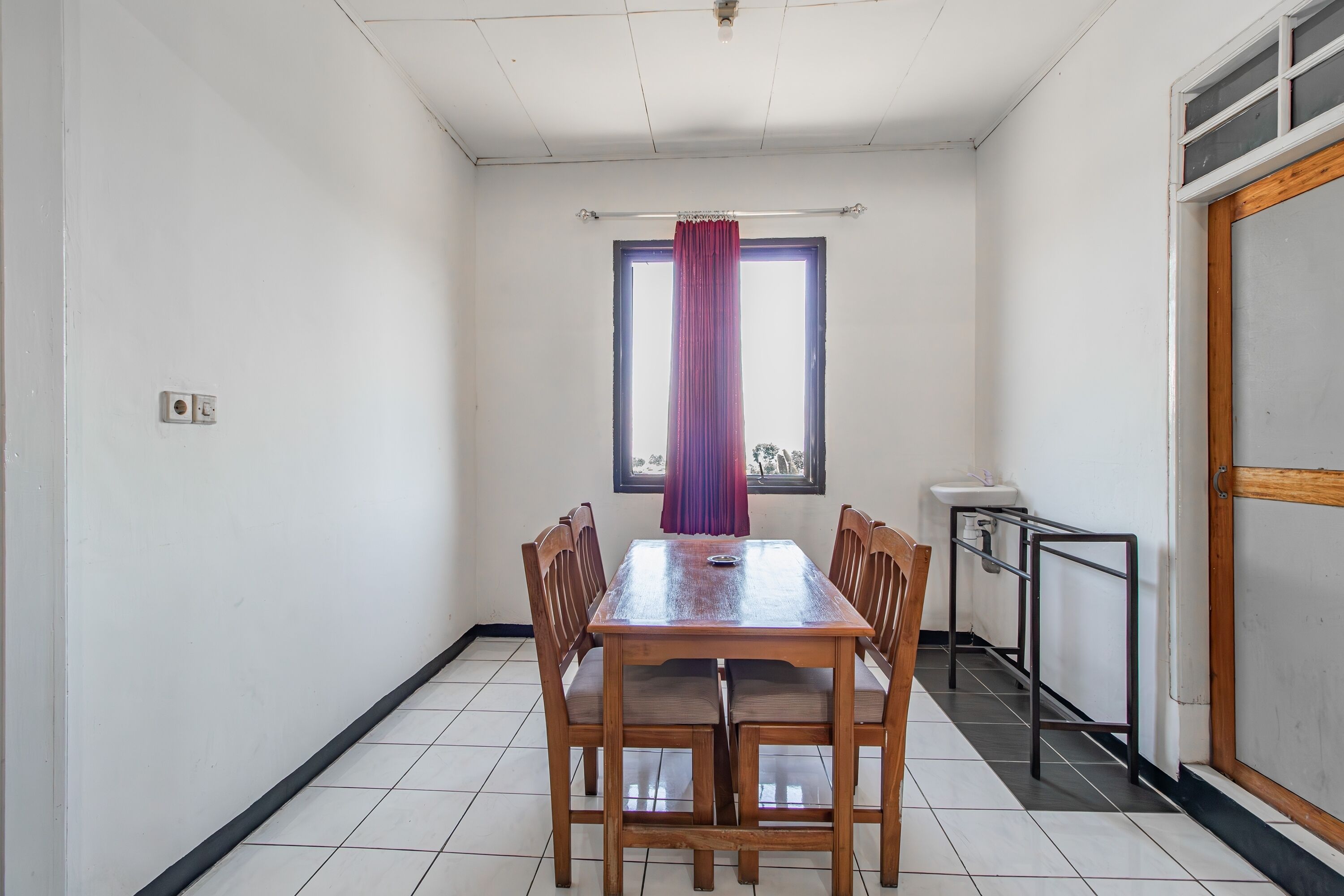 A room with a dining table, chairs, a window with curtains, a sink, and a tiled floor.