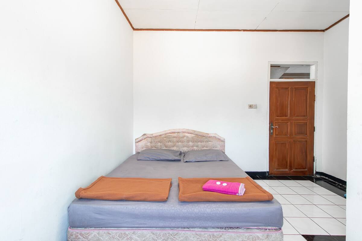 Een kleine, eenvoudige kamer met een bed, een houten deur en een betegelde vloer.