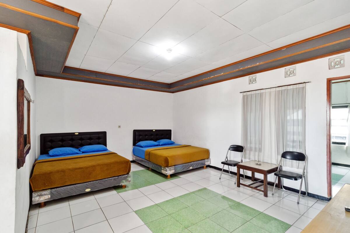 Een hotelkamer met twee bedden, een tafeltje, twee stoelen en een raam met gordijnen.