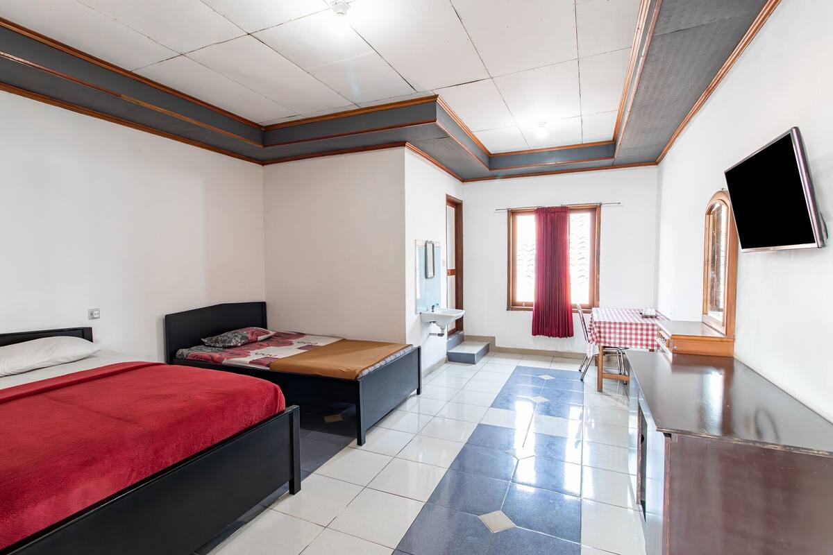 Hotelkamer met een bed, bureau, stoel, televisie, raam met gordijnen en een badkamer.