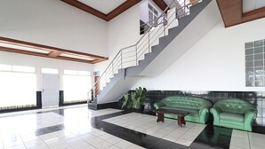 Un hall d’entrée spacieux avec un escalier, des canapés verts et un sol carrelé.
