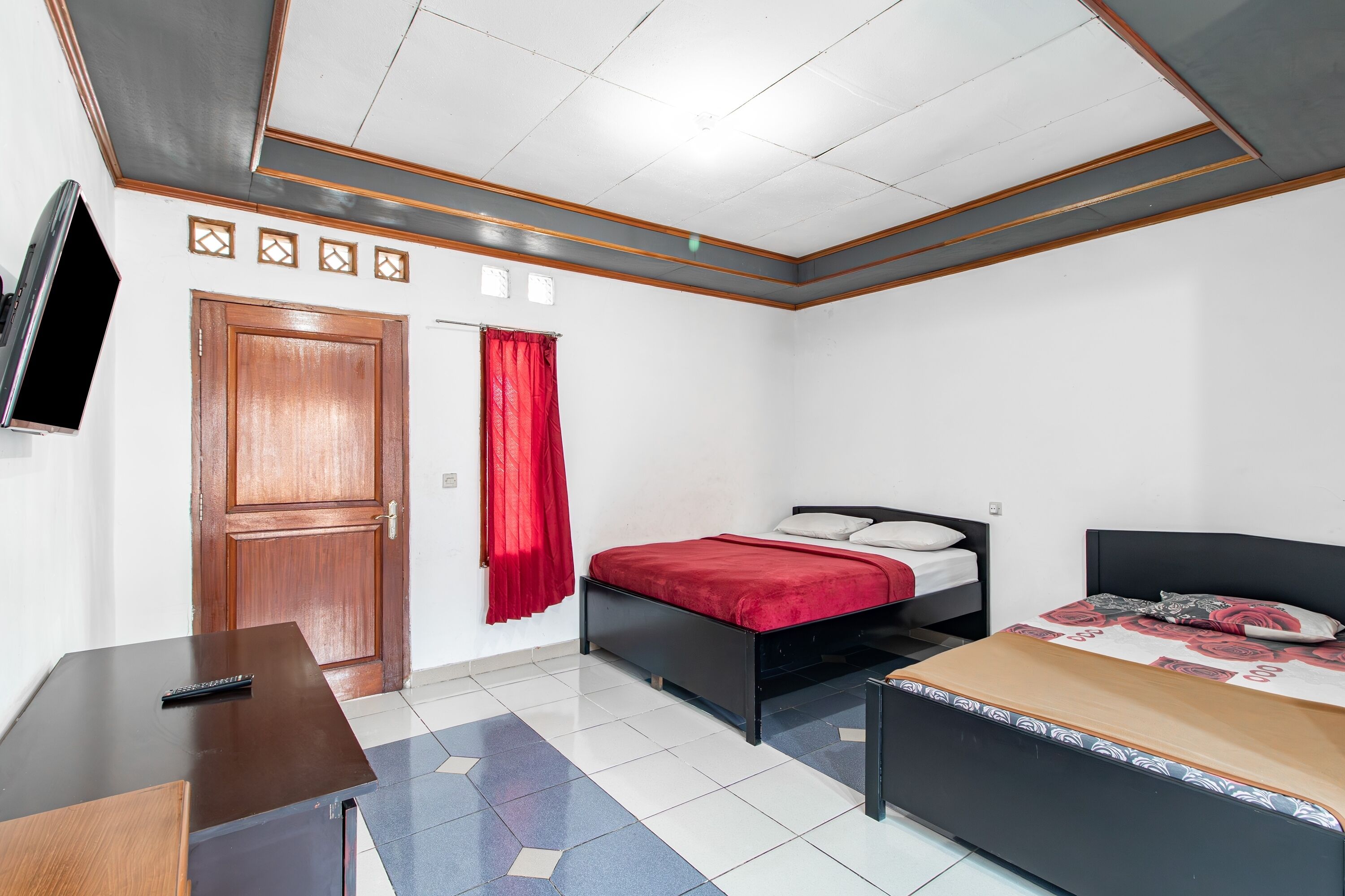 A bedroom with two beds, a TV, a wooden door, and a red curtain.