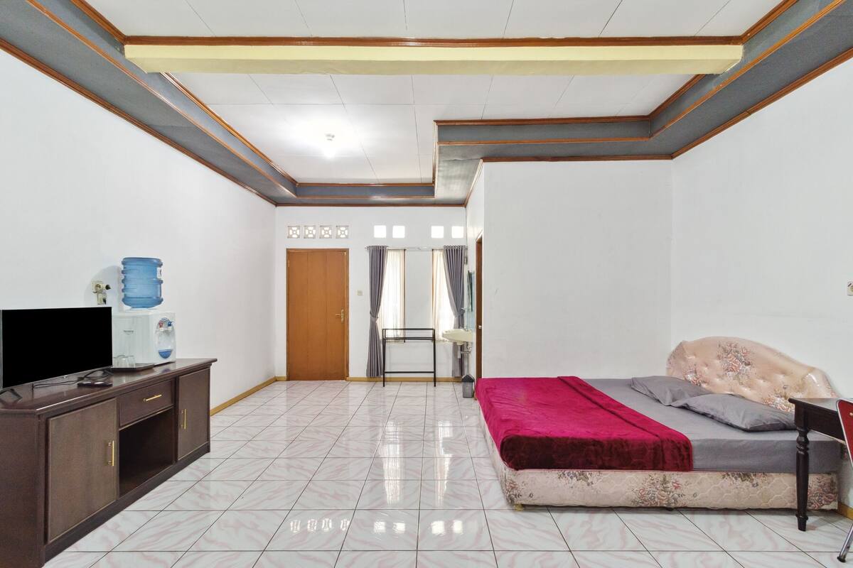 Een slaapkamer met een bed, een televisie, een waterdispenser en een deur naar een andere kamer.