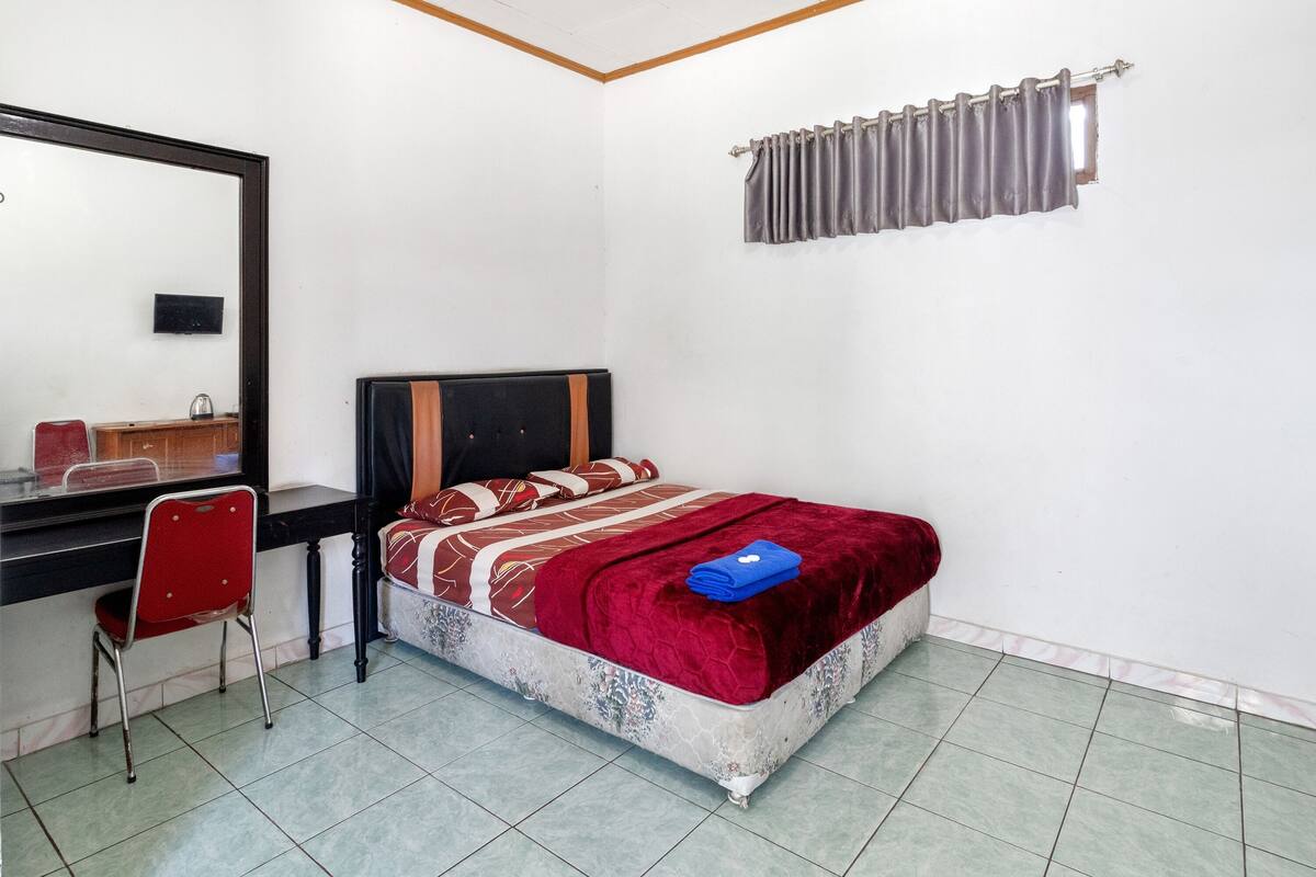 Een slaapkamer met een bed, een bureau, een stoel en een raam met gordijnen.