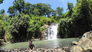 Una persona de pie sobre rocas junto a una cascada en un área boscosa.