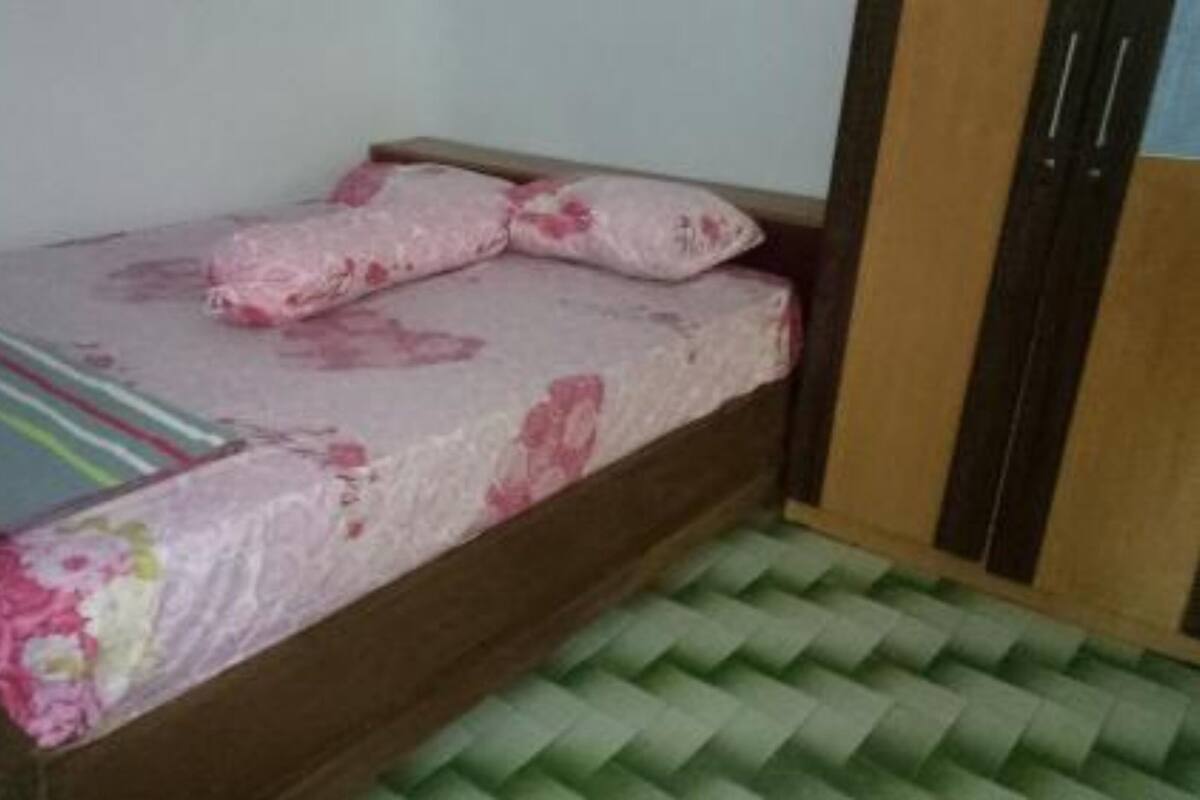 A small, single-bed room with a wooden bed frame, a floral bedspread, and a green patterned rug.
