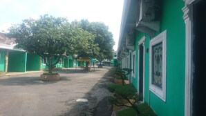 A street lined with green buildings, some with white trim, and trees in the foreground. - Hotel Bukit Panembahan (Durin Simbelang)