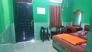 A room with a bed, a wooden nightstand, a chair, a mirror, and a door. - Hotel Bukit Panembahan (Durin Simbelang)